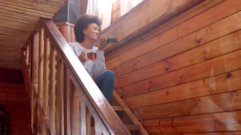 feliz mujer afroamericana hablando en el teléfono inteligente y bebiendo té en las escaleras, en cámara lenta