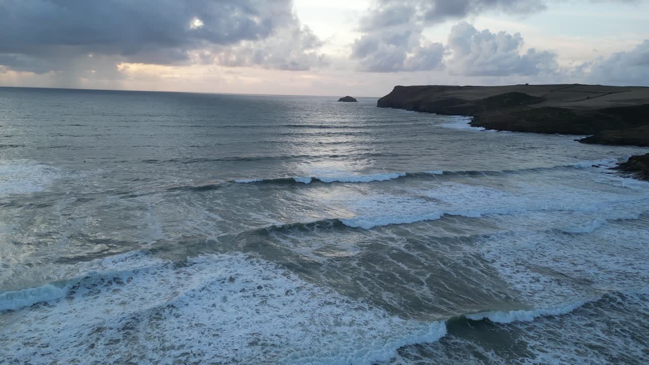 Drone video capturing Polzeath Beach's serene waves under dramatic skies. Aerial footage showcases stunning coastal landscape with dynamic cloud formations and glistening sea water