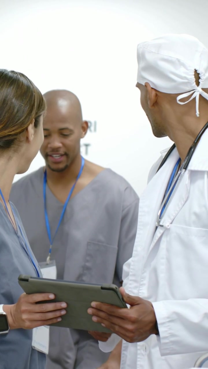 Vertical video: Approaching tech handing tablet, white coat MD, gray scrubs reviewing orders by MRI