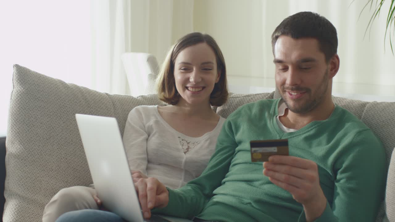 una pareja está sentada en el sofá y haciendo compras en línea usando una tarjeta de crédito.