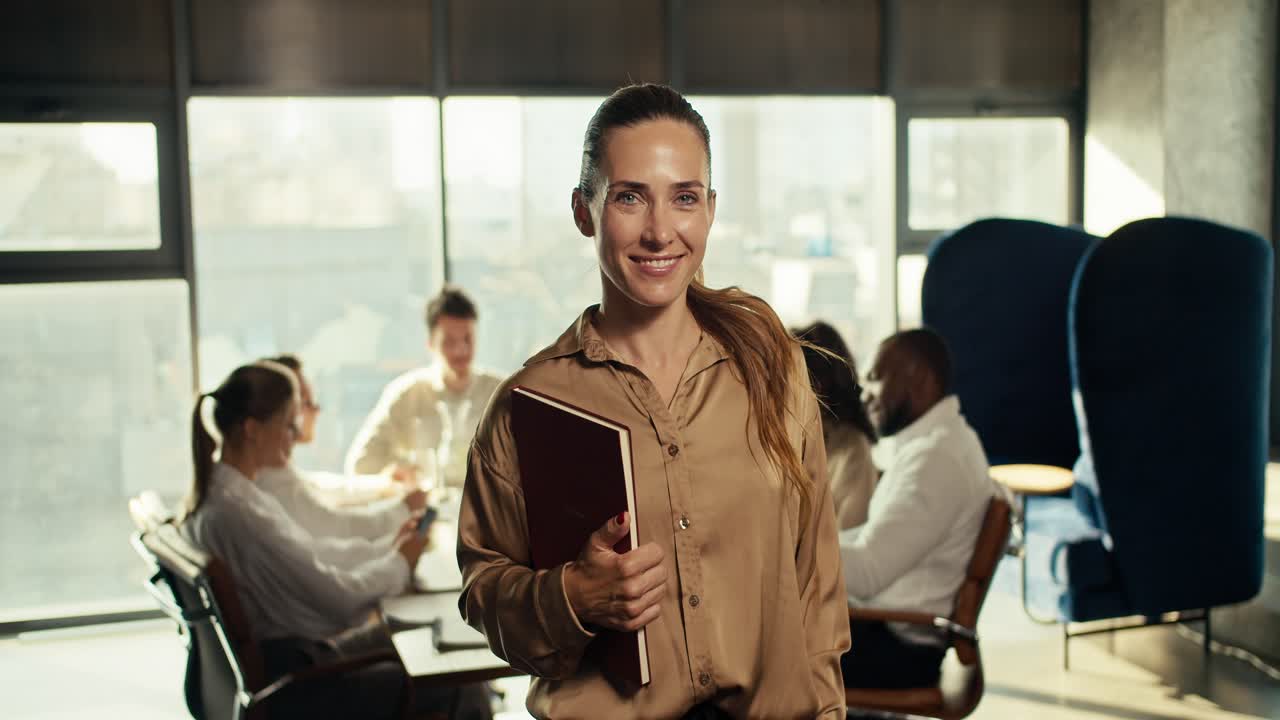 feliz mujer de negocios exitosa en negocios ropa marrón sonriendo mirando a la cámara en la oficina. contra el telón de fondo de los trabajadores de la oficina