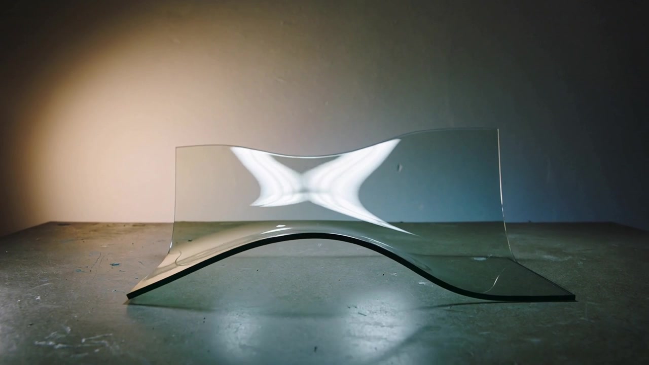 Et gennemsigtigt ark trækkes op til et opretstående panel i et studie, hvilket afslører vingelignende højdepunkter fra en lampe.
