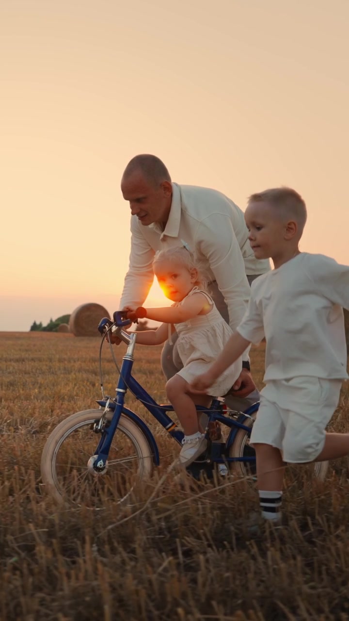 Padre che insegna alla figlia ad andare in bicicletta in un campo al tramonto