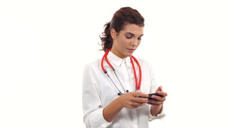 Porträt-Einer-Jungen-Krankenschwester,-Die-Ihr-Smartphone-Zum-Senden-Von-Textnachrichten-Nutzt.-Junger-Mediziner-Mit-Stethoskop-Und-Laborkittel-Isoliert-Auf-Weißem-Hintergrund