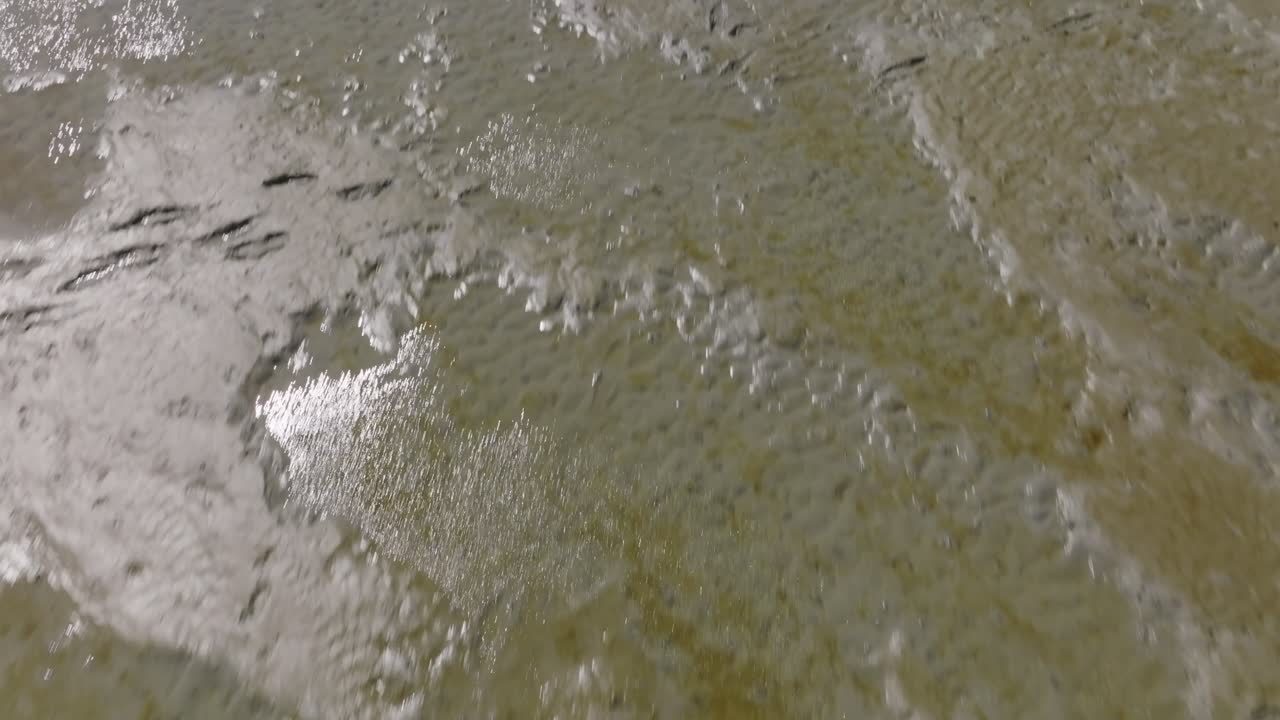 Wet Wadden Sea mudflat at low tide shown in a true vertical overhead; drone captures rippled sediment texture and water sheen without horizon