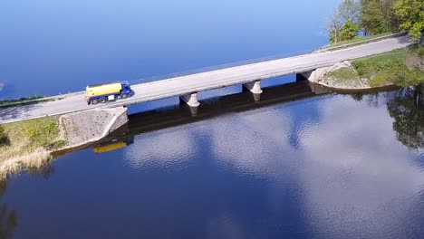 aerial shot of a fuel truck driving on a bridge over a lake