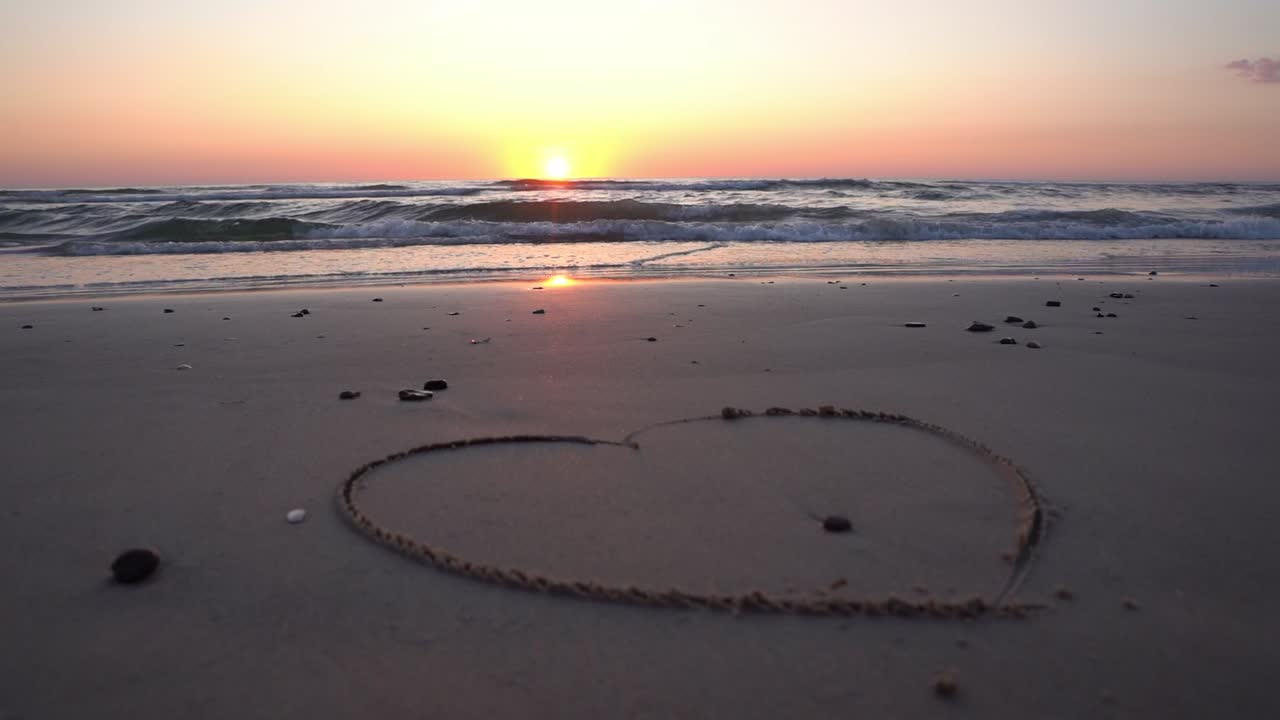 바다 위에 해가 지는 배경에 모래에 그려진 심장 기호