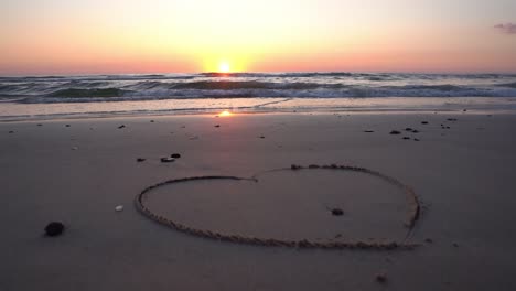 símbolo de corazón dibujado en la arena contra un telón de fondo de puesta de sol sobre el mar