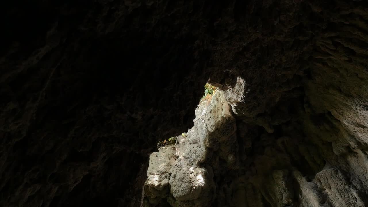 Visuale dal basso di un foro nel tetto di una grotta di pietra nel giardino nasride di Vélez de Benaudalla, che lascia entrare la luce del sole e mostra la vegetazione esterna