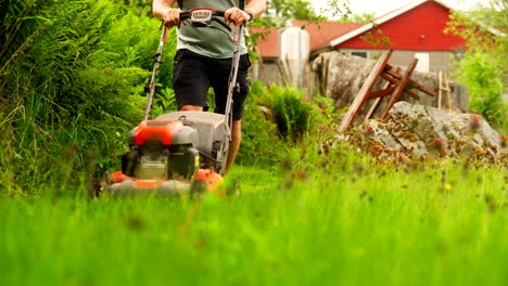 Low angle frontal view of overgrown lawn being mowed using petrol lawnmower