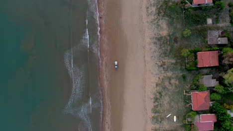 aerial top down shot of one car driving along an empty sandy beach