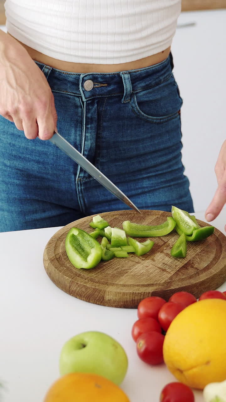 The girl cuts with a knife a green bell pepper. Table with vegetables and fruits for a healthy diet. Vertical video