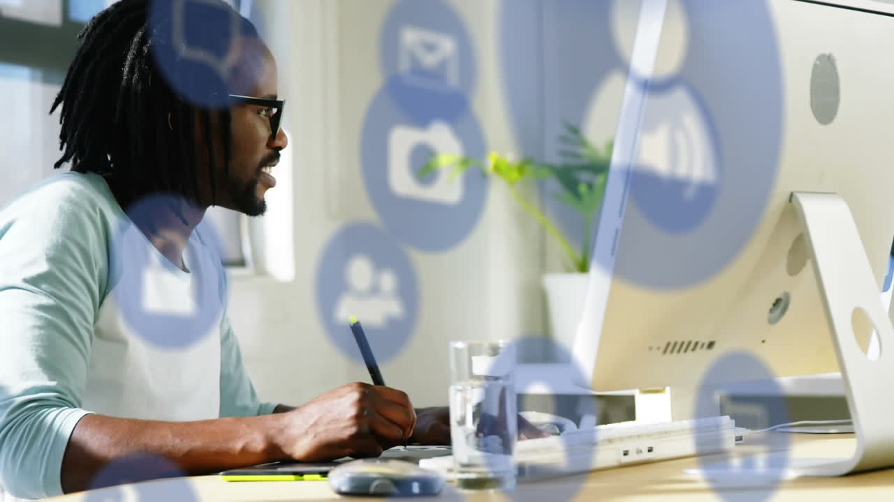 Animation of digital icons over african american man using graphic tablet at office