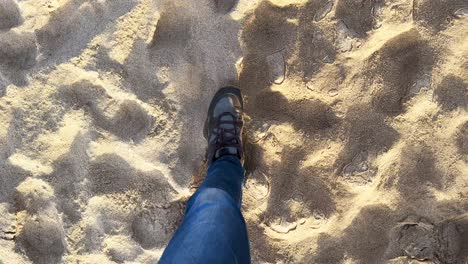 cinematic shot of a person walking over sand looking down