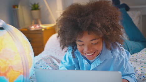retrato de un niño en el dormitorio acostado en la cama usando una computadora portátil con un globo iluminado