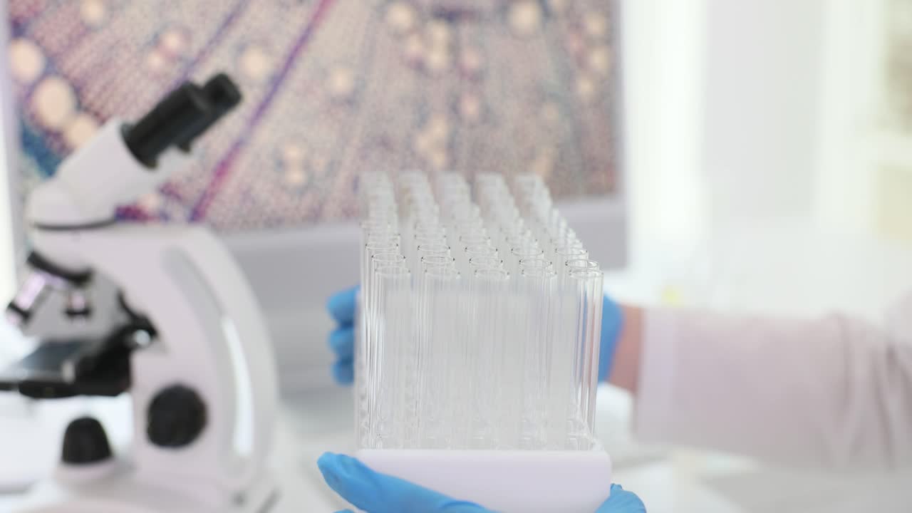 Gloved hands holding test tubes in a laboratory with a microscope