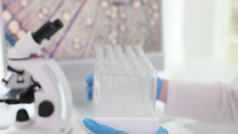 gloved hands holding test tubes in a laboratory with a microscope