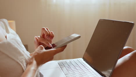 woman using a smartphone and laptop in bed