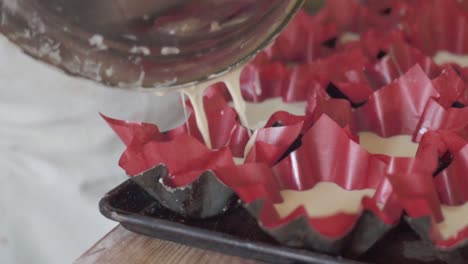 primer plano de un chef de pastelería vertiendo masa en forros de pasteles para hornear