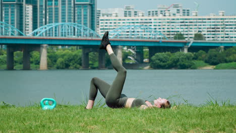 young woman performing single leg glute bridge exercise while training in seoul city han river park with dongjak bridge in background - side view