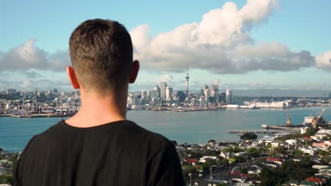 young caucasian man looking at auckland skyline from devonport, new zealand