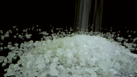 camera dolly forward - coarse salt falling on a black mirrored surface