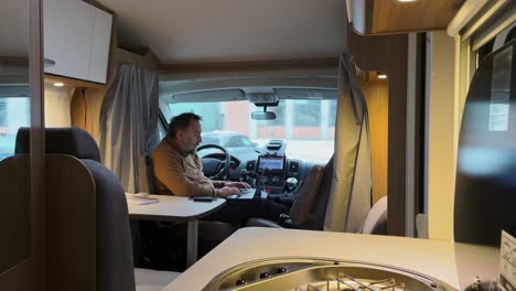 Senior-man-or-digital-nomad-working-laptop-in-campervan,-winter-and-rain-outside,-vanlife-concept