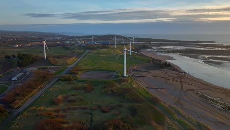 wind turbines moving at different speeds on coastal wind farm at sunset golden hour