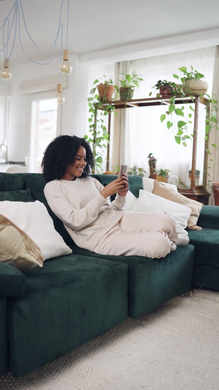 Donna afroamericana felice che si rilassa sul divano e usa lo smartphone