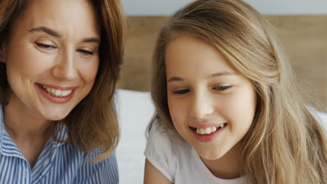 young beautiful mother lying on the bed with her daughter and talking in the morning