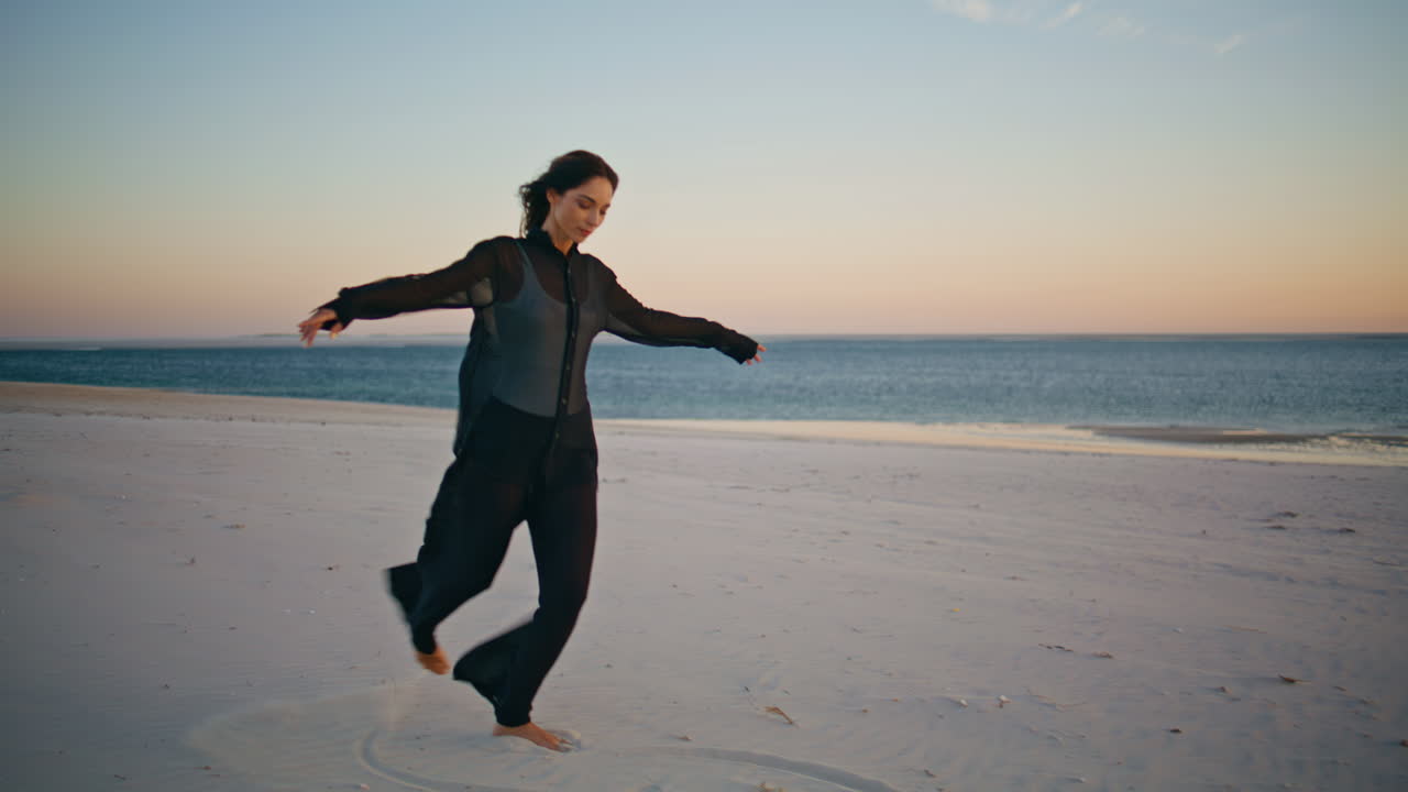 Serene woman dancing barefoot on scenic sunset beach. Carefree lady at evening
