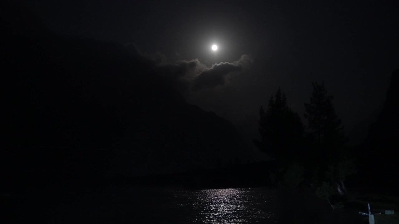 Bulan purnama bersinar di atas danau gunung yang gelap, memancarkan pantulan cahaya terang di seluruh permukaan air.