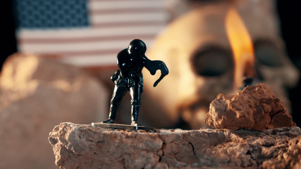 Soldatino di plastica che si scioglie dal calore in un diorama di scena di guerra. Teschi umani e una bandiera americana sono visibili sullo sfondo sfocato
