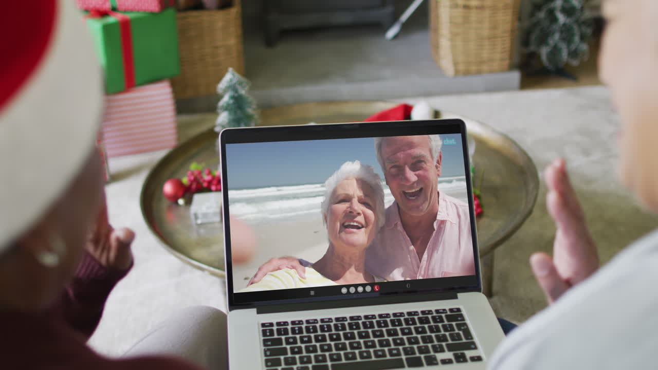 diversas amigas mayores que usan una computadora portátil para una videollamada de navidad con una pareja feliz en la pantalla