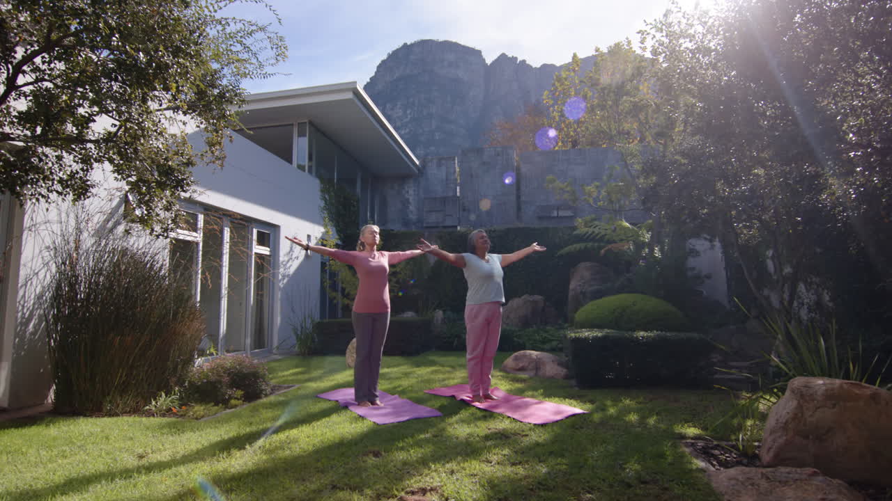 Practicing yoga outdoors, two multiracial female friends stretching on yoga mats in garden