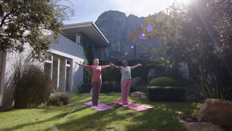 practicing yoga outdoors, two multiracial female friends stretching on yoga mats in garden