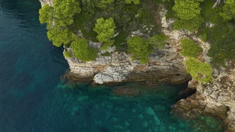 Kalamota-Island,-Adriatic-Sea,-Croatia---Clear-Blue-Waters-Contrast-with-the-Rugged-Shoreline-Below-the-Vegetated-Rock-Cliffs---Aerial-Drone-Shot