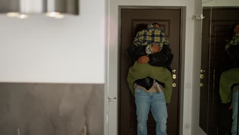 A-happy-young-brunette-girl-with-a-bob-hairstyle-in-a-plaid-shirt-runs-and-hugs-her-young-boyfriend-with-Black-skin-a-brunette-in-a-black-jacket-who-came-home-and-after-work-in-the-evening