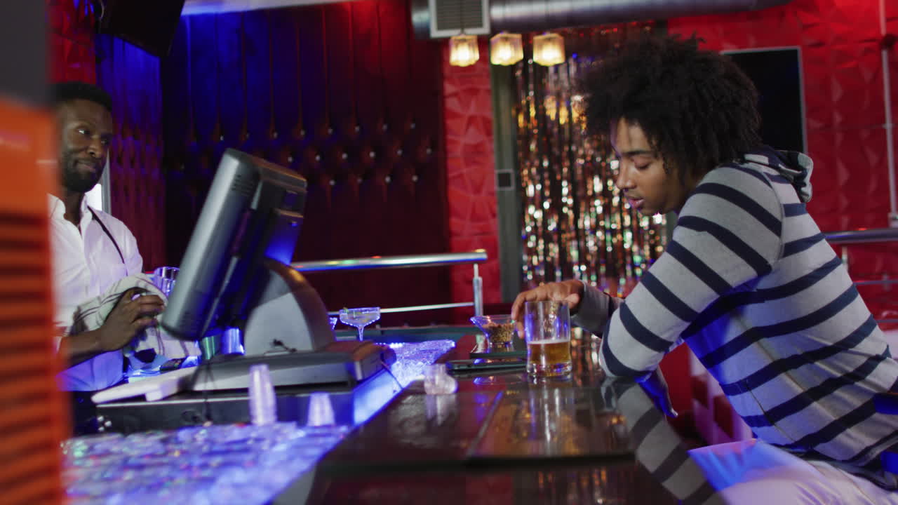 video di un barista afroamericano sorridente e di un uomo ubriaco seduto a bere birra al bar