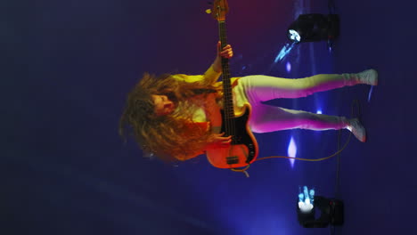 Vertikales-Video-Einer-Springenden-Lustigen-Frau-Mit-Einer-Gitarre-In-Einem-Studio-Im-Neonlicht