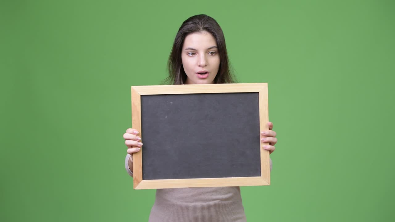 Young beautiful woman looking shocked while holding blackboard