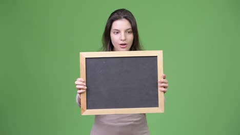 young beautiful woman looking shocked while holding blackboard