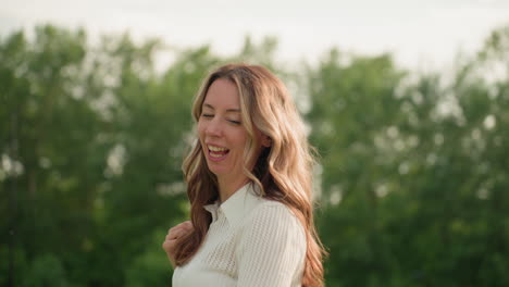 young mom smiling walking with child, chatting, wind brushing through long hair, park background, warm light, casual outing, warm sunlight highlighting joyful expression and relaxed afternoon mood