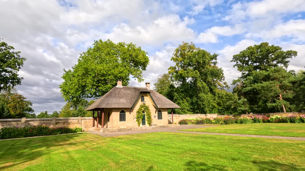 Wide-angle tracking shot of a thatched-roof cottage amid lush garden, trees, and winding path