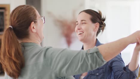 pareja de lesbianas caucásicas sonriendo y bailando en la cocina