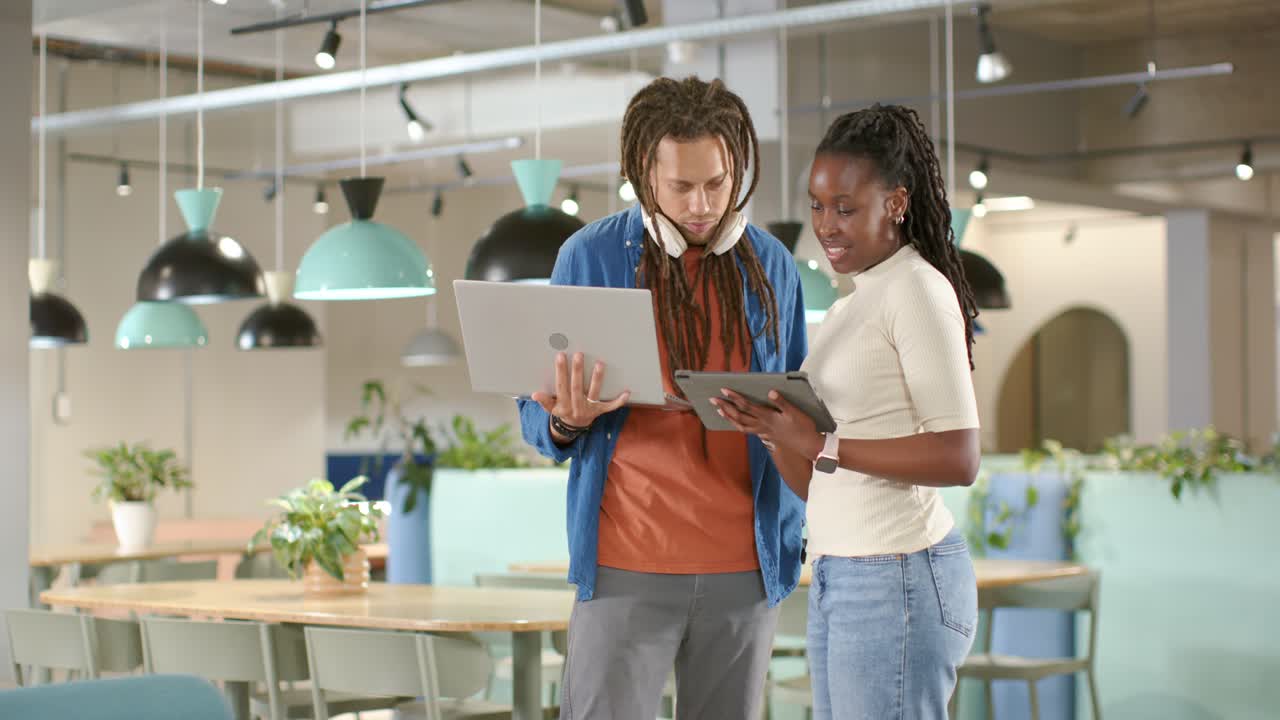 Kollegene starter prosjektgjennomgang i et co-working space, lener seg, trykker på nettbrettet og justerer bærbar PC