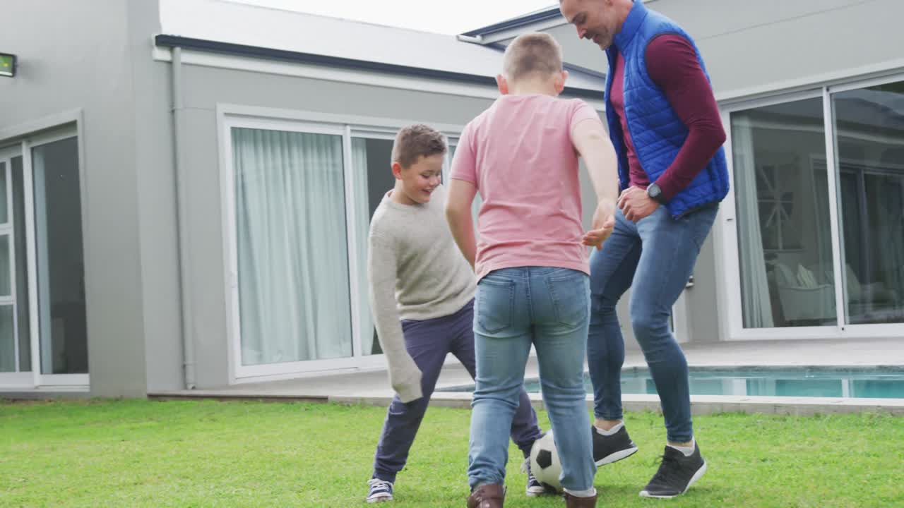 Gelukkige blanke vader met twee zonen die voetbal spelen in de tuin.