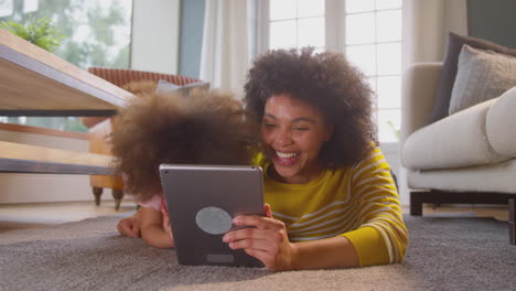 Mother-And-Daughter-Having-Fun-Lying-On-Floor-Streaming-Movie-On-Digital-Tablet-At-Home-Together