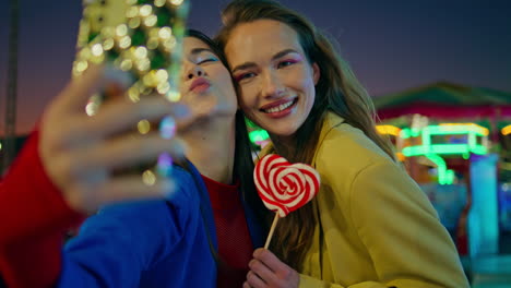 joyful friends making selfie at night luna park closeup. happy girls at funfair