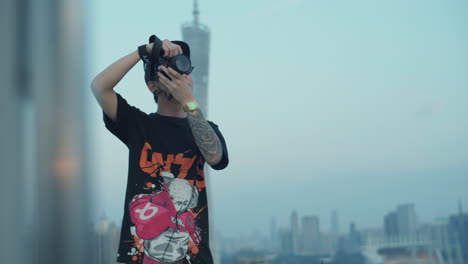 young asian photographer with tattoo captures urban downtown cityscape from the rooftop in the early morning